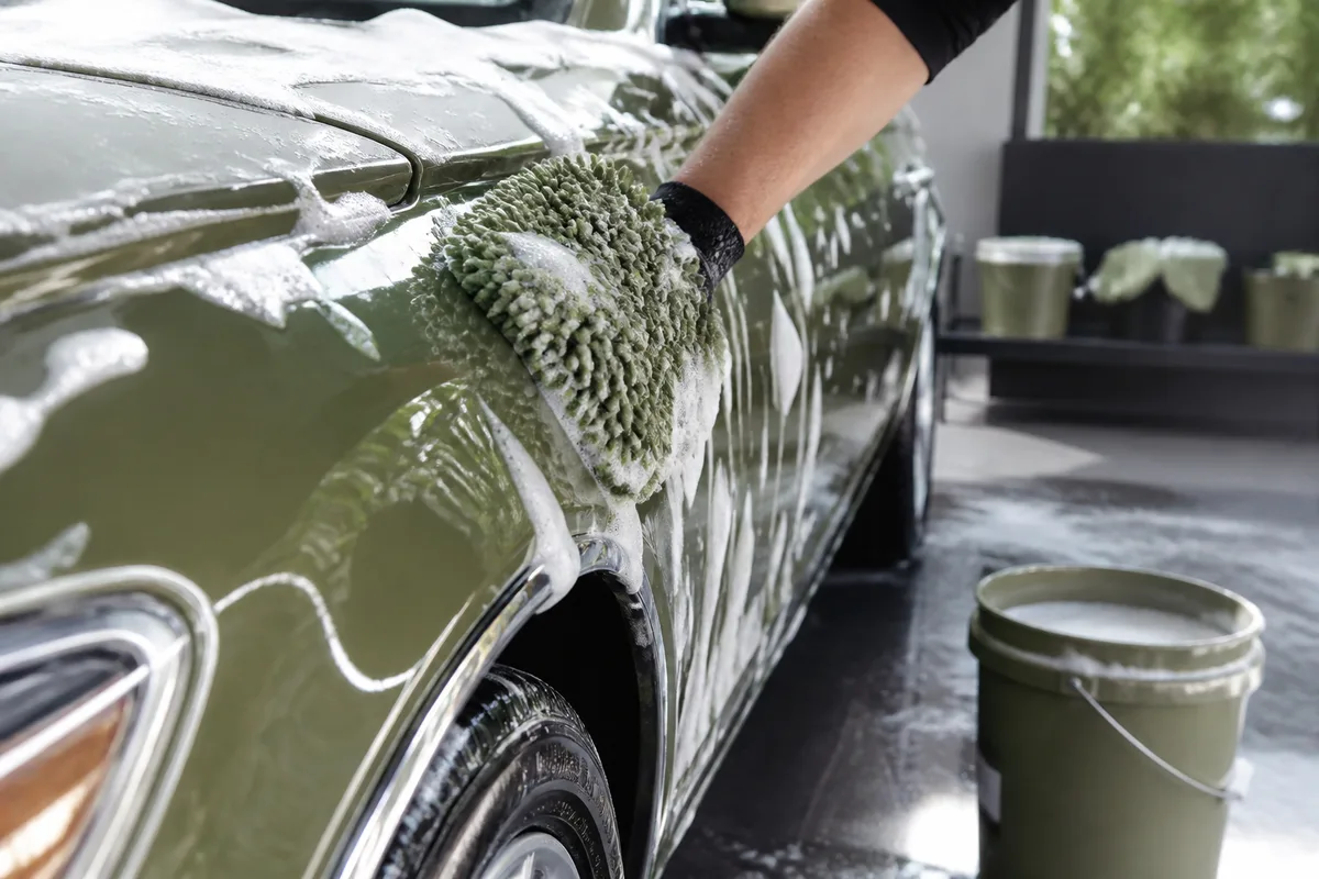 Lavage manuel d’une carrosserie avec gant en microfibre et seau posé au sol