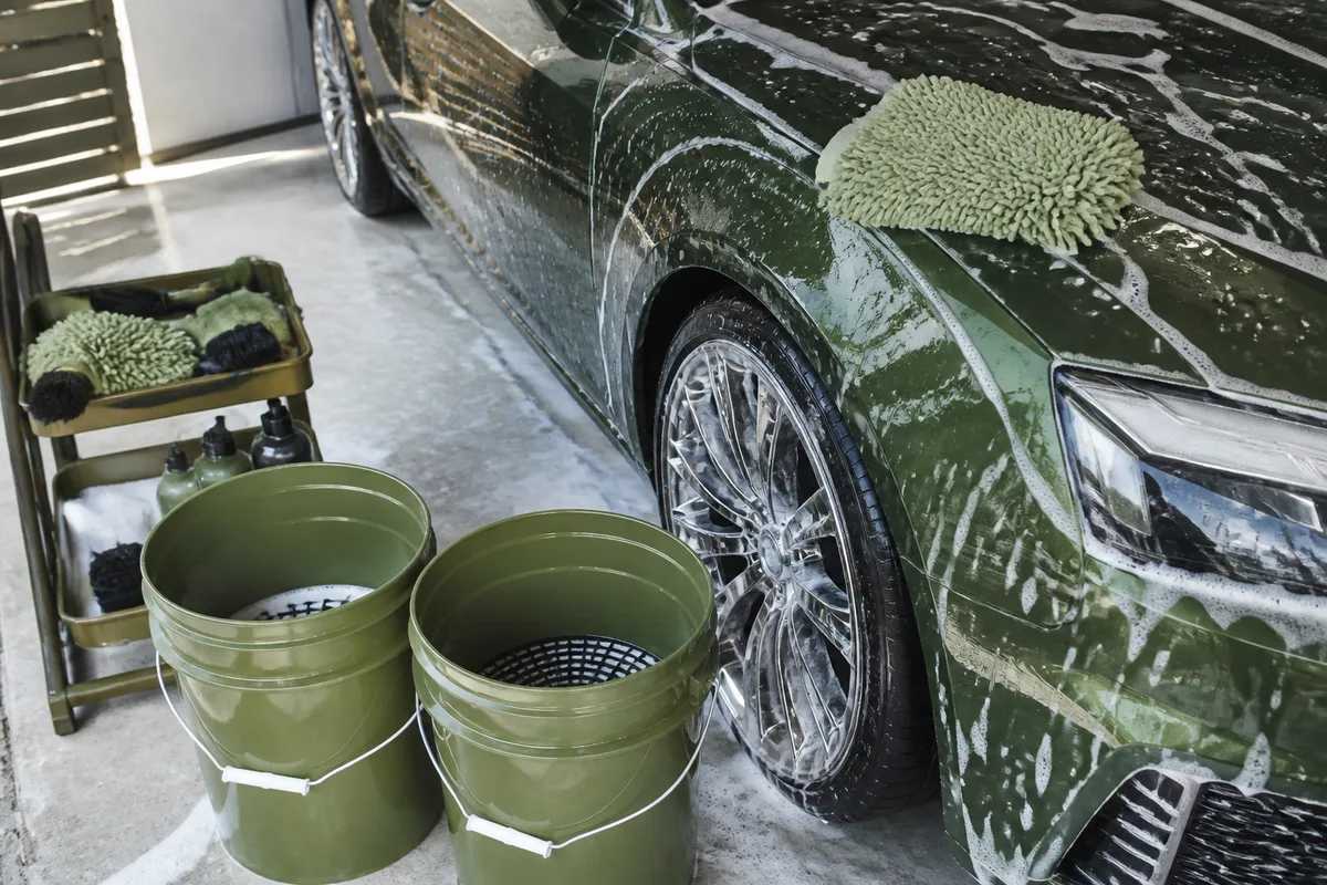 Deux seaux de lavage avec grille de fond et gant en microfibre posé sur une aile de voiture propre