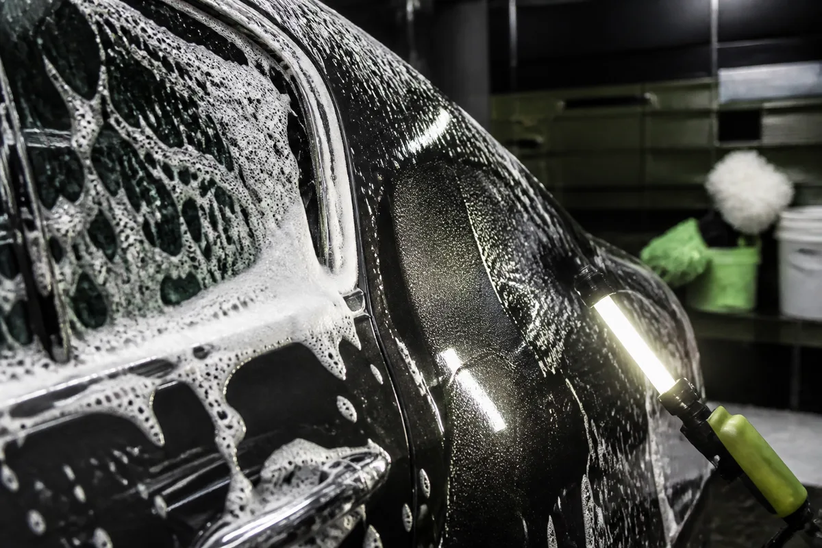 Détail d’une carrosserie sombre haut de gamme éclairée par une lampe d’inspection en atelier